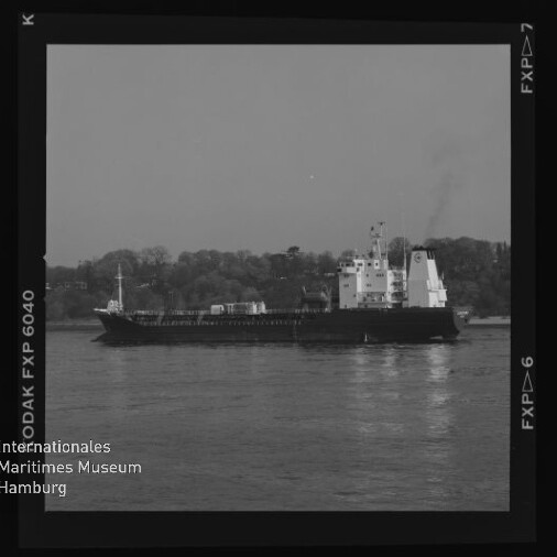 Frachtschiff auf ruhigem Fluss vor bewaldeter Uferlinie; Bildrand zeigt Logo Maritimes Museum Hamburg.