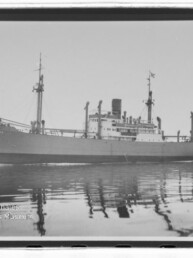 Großes Frachtschiff mit Schornstein und Masten fährt auf spiegelglattem Meer, Reflexion sichtbar.