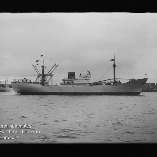 Frachtschiff mit Ladekränen und Schornstein fährt auf ruhigem Wasser, Hafenbebauung im Hintergrund und Museumslogo links unten.
