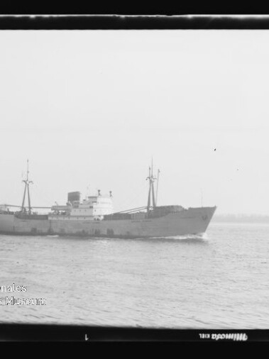 Schwarzweiß-Foto eines Frachtschiffs im Seitenprofil auf ruhiger See, Filmrand und Museumslogo links unten.