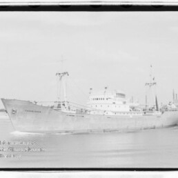 Schwarzweißfoto des Frachtschiffs CASABLANCA mit Ladekränen auf ruhigem Wasser vor der Küste; Museumssiegel unten links.