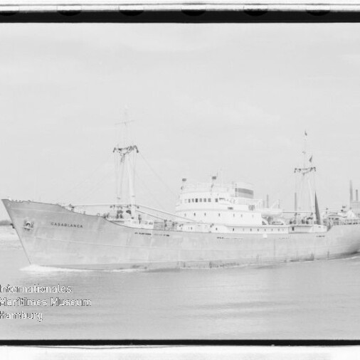 Schwarzweißfoto des Frachtschiffs CASABLANCA mit Ladekränen auf ruhigem Wasser vor der Küste; Museumssiegel unten links.