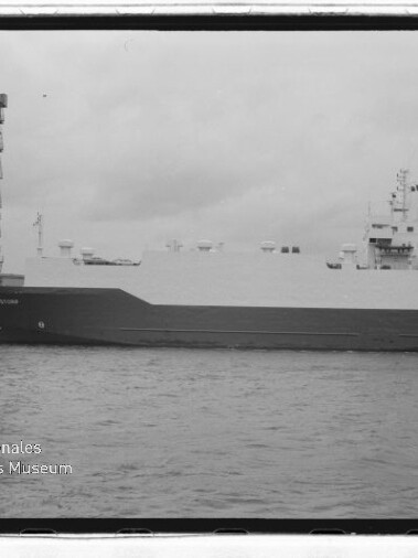 Großes weißes Ro‑Ro‑Frachtschiff am Kai unter bedecktem Himmel, links ein Hafenkran und unten links ein Museumswasserzeichen.