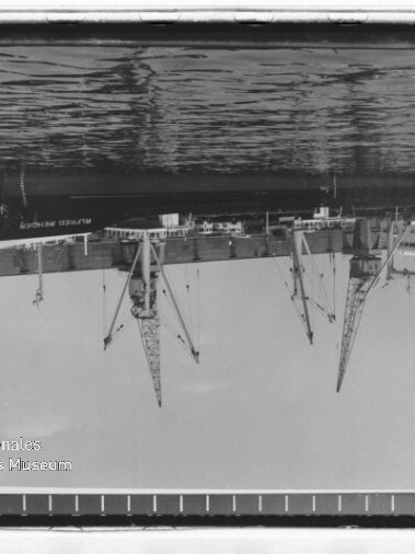 Auf dem Kopf stehendes SW-Foto eines Hafens mit Kränen, angedocktem Schiff und dem Logo Internationales Maritimes Museum Hamburg
