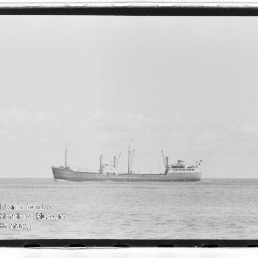 Schwarzweißfoto eines Frachtschiffs auf ruhiger See, Schiff mittig am Horizont, Museumswasserzeichen unten links.