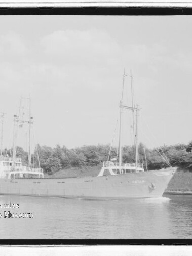 Zweimastiges Frachtschiff auf ruhigem Kanal vor Bäumen, mit Wasserzeichen des Internationalen Maritimen Museums Hamburg.