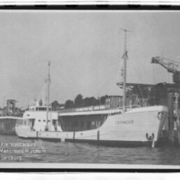 Schiff Cepheus am Kai eines Industriehafens, Bug mit Namen sichtbar, Kran und Piergebäude im Hintergrund.