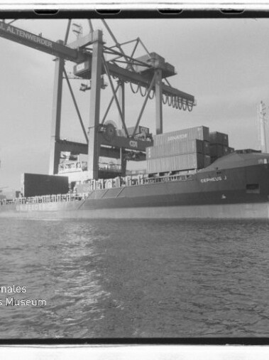 Frachtschiff am Kai mit Containern und Hafenkranen; Siegel des Internationalen Maritimen Museums Hamburg sichtbar.