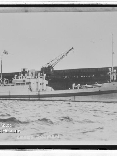 Frachtschiff am Kai unter zwei großen Kränen, seitliche Ansicht vom Wasser mit ruhiger See