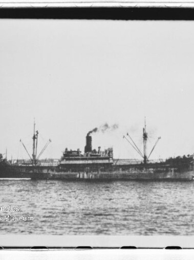 Dampffrachtschiff mit rauchendem Schornstein und Ladebäumen, kleines Begleitschiff, Wasser und Küste; Museumslogo links unten.