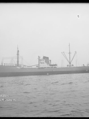 Frachtschiff im Hafen vor Krananlagen, leicht neblige Sicht; Schriftzug Internationales Maritimes Museum Hamburg unten links.