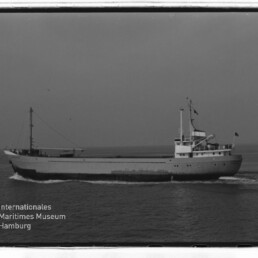 Frachtschiff seitlich mit Brücke und Flaggen auf ruhiger See; Wasserzeichen Internationales Maritimes Museum Hamburg