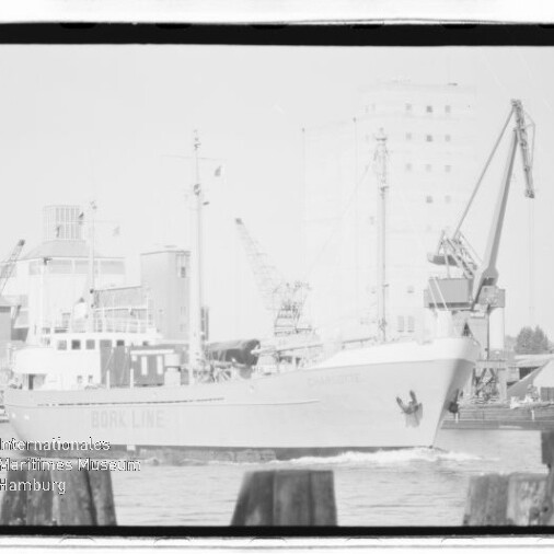 Schwarzweiß-Aufnahme eines Frachtschiffs mit Schriftzug NORDLINE, das an einem Hafen mit Kränen und Silos vorbeifährt.