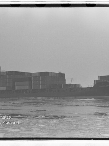 Containerschiff mit gestapelten Containern auf ruhiger See; schwarzweißes Foto mit Wasserzeichen des Maritimen Museums.