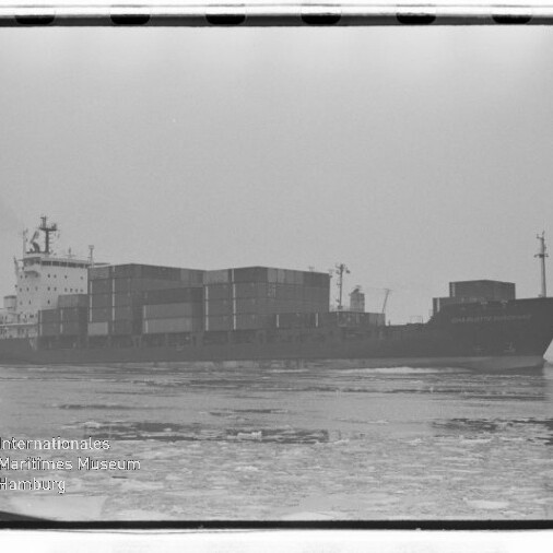Containerschiff mit gestapelten Containern auf teils zugefrorenem Meer in Nebel, Wasserzeichen Int. Maritimes Museum Hamburg.