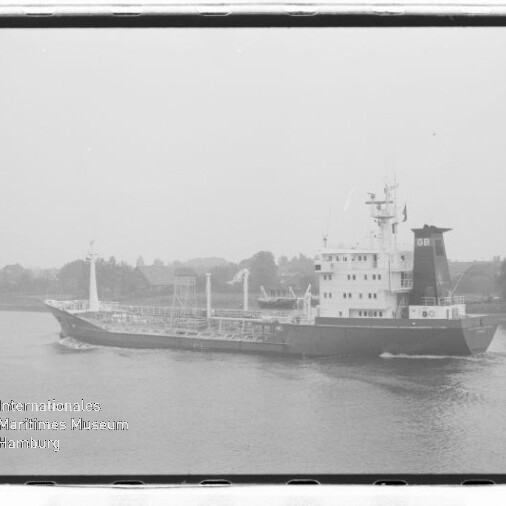 Schwarzweißfoto eines Tankschiffs auf ruhigem Wasser vor einem baumbestandenen Ufer, Museum-Logo unten links.