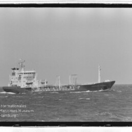 Schwarzweißaufnahme eines Tankers mit Aufbau achtern und Rohrleitungen auf offener See; unten links Museumswasserzeichen.