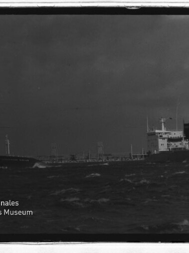 Frachtschiff auf rauer See unter dunklem Himmel; links unten das Logo Internationales Maritimes Museum Hamburg.