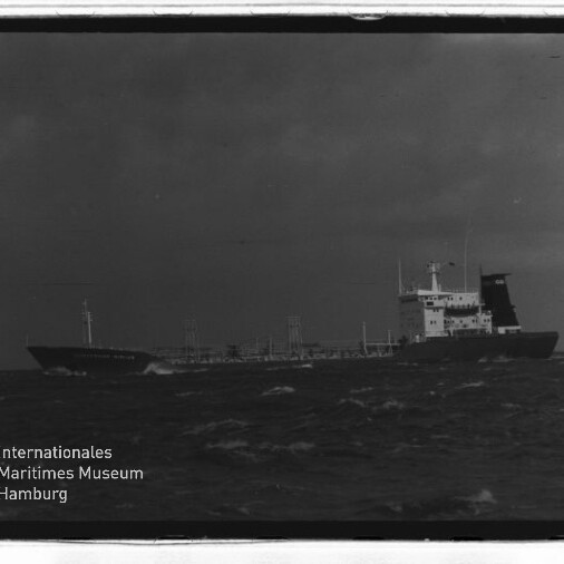 Frachtschiff auf rauer See unter dunklem Himmel; links unten das Logo Internationales Maritimes Museum Hamburg.