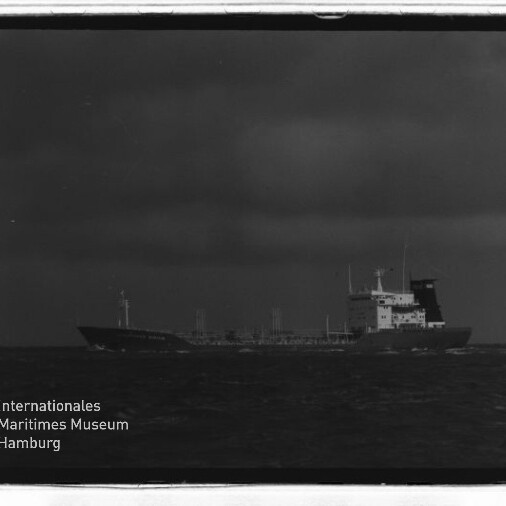 Schwarzweißfoto eines Tankschiffs auf rauer See unter dunklen Wolken, Museumslogo unten links
