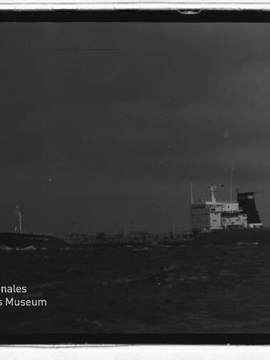 Schwarzweiß-Frachtschiff mit Heckaufbau und Schornstein auf See; unten links Logo Maritimes Museum Hamburg.