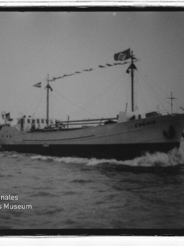 Schwarzweißfoto eines Frachtschiffs mit Flaggen auf See; Schriftzug Internationales Maritimes Museum sichtbar.