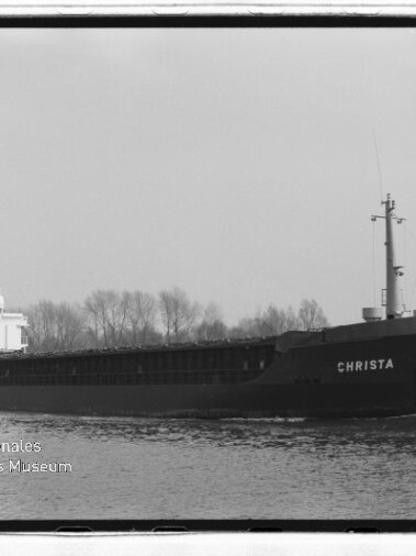 Schwarzweißaufnahme eines Frachtschiffs namens CHRISTA auf ruhigem Kanal, Ufer mit kahlen Bäumen und Museumswasserzeichen.
