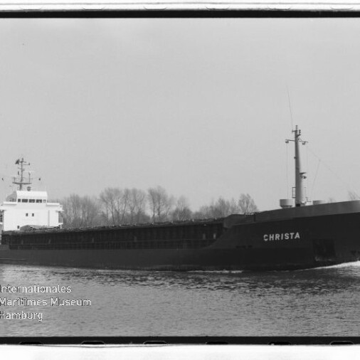 Schwarzweißaufnahme eines Frachtschiffs namens CHRISTA auf ruhigem Kanal, Ufer mit kahlen Bäumen und Museumswasserzeichen.