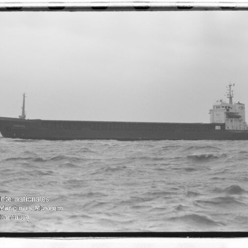 Langes Frachtschiff in Seitenansicht auf leicht welliger See, Museumswasserzeichen unten links.
