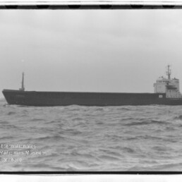 Langes Frachtschiff auf bewegter See unter grauem Himmel, mit Internationales Maritimes Museum Hamburg‑Wasserzeichen unten links.