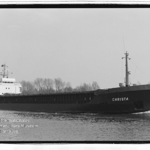 Frachtschiff CHRISTA auf einem Kanal, seitlich zu sehen, dunkler Rumpf, weiße Aufbauten und Baumreihe im Hintergrund.
