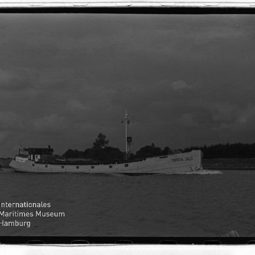 Weißes Frachtschiff mit lesbarem Namen CHRISTA 383 fährt vor Küstenlinie unter dunkler Wolkendecke; Museumslogo unten links.