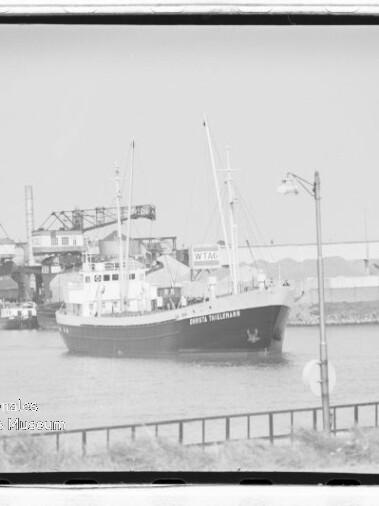 Kleiner Frachter mit zwei Masten im Industriehafen vor Krananlagen; Wasserzeichen 