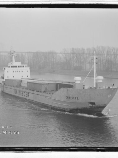 Frachtschiff Christel mit Unifeeder-Schriftzug fährt einen Fluss entlang; Brücke und Uferbäume im Nebel.