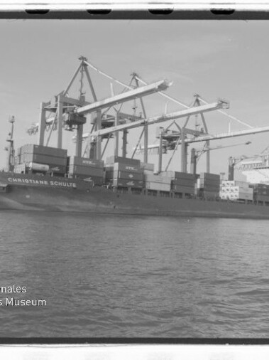 Containerschiff CHRISTIANE SCHULTE am Kai unter großen Hafenkränen, Containerstapeln und Wasser vorn; Museumslogo sichtbar.