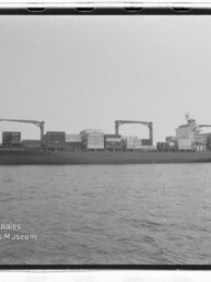 Frachtschiff mit Containern und zwei Ladekränen auf ruhiger See; Wasserzeichen des Internationalen Maritimen Museums Hamburg.