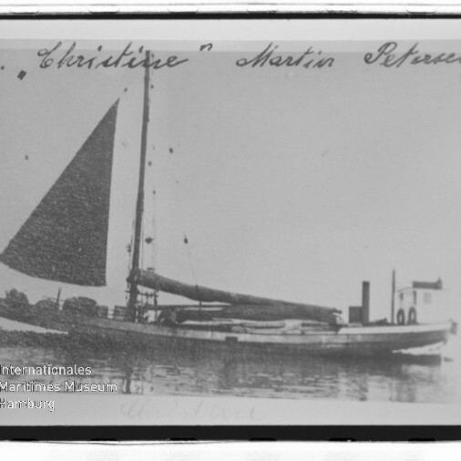 Ein kleines Einmast-Segelschiff mit aufgeholtem dreieckigem Segel liegt ruhig im Wasser, oben ist ein handschriftlicher Schriftzug sichtbar.