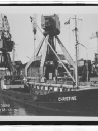 Schwarzweißaufnahme des Frachtschiffs CHRISTINE am Kai mit großen Hafenkränen und Silos im Hintergrund.
