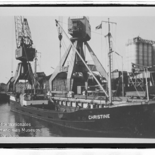 Schwarzweißaufnahme des Frachtschiffs CHRISTINE am Kai mit großen Hafenkränen und Silos im Hintergrund.