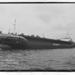 Schwarzweißfoto eines Frachtschiffs mit Namen CHRISTOPHER und Schriftzug ECHOSHIP, längsseits am Kai, Wasser im Vordergrund.