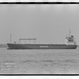 Frachtschiff mit Aufschrift GENESIS fährt auf ruhiger See vor einem Hafen, schwarz-weiß, Museumslogo unten links.