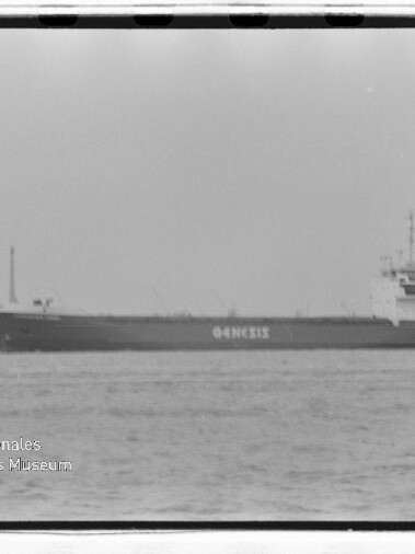 Frachtschiff mit Schriftzug GENESIS auf ruhiger See, Hafenkran im Hintergrund, schwarzweißfotografie.