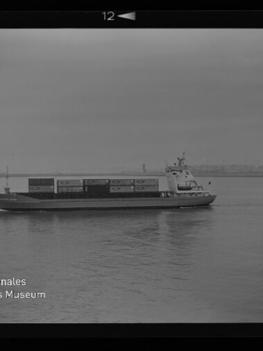 Containerschiff seitlich auf ruhiger See mit auf Deck gestapelten Containern und flachem Küstenhorizont
