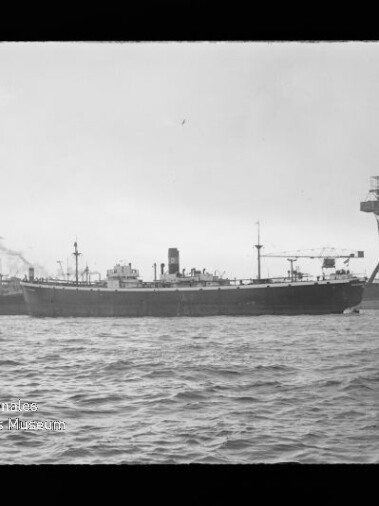 Großes Frachtschiff im Hafen, Wellen im Vordergrund und ein hoher Kran am rechten Ufer; Wasserzeichen: Maritimes Museum Hamburg.