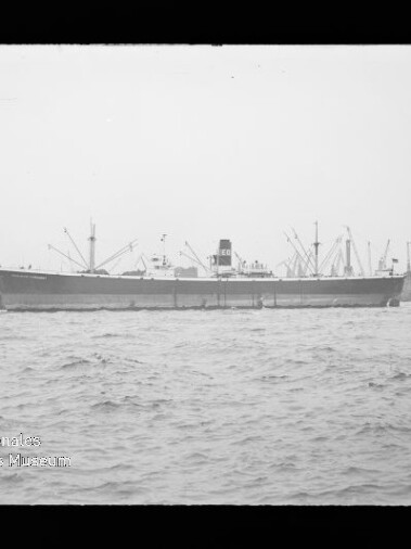 Großes Frachtschiff an der Kaimauer mit Hafenkränen im Hintergrund und unruhiger See im Vordergrund.