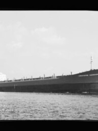 Großes Massengutfrachtschiff mit langem flachen Rumpf und Achterbrücke fährt auf ruhiger See; schwarz-weißes Foto.