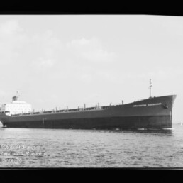 Großes Massengutfrachtschiff mit langem flachen Rumpf und Achterbrücke fährt auf ruhiger See; schwarz-weißes Foto.