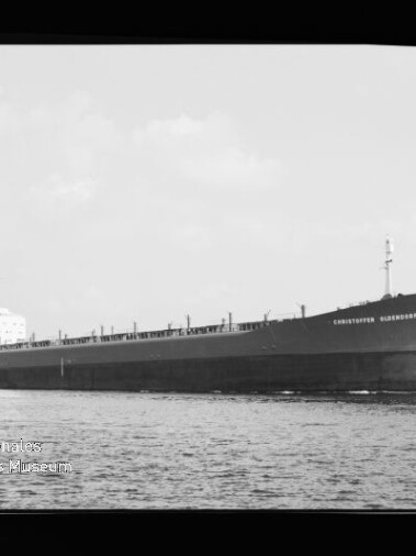Großes Massengutfrachtschiff mit langem flachen Rumpf und Achterbrücke fährt auf ruhiger See; schwarz-weißes Foto.