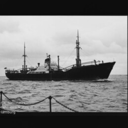 Frachtschiff mit Masten und Ladekränen auf welliger See, bewölkter Himmel; Wasserzeichen Maritimes Museum Hamburg unten links.
