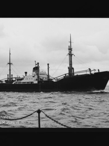 Frachtschiff mit Masten und Ladekränen auf welliger See, bewölkter Himmel; Wasserzeichen Maritimes Museum Hamburg unten links.
